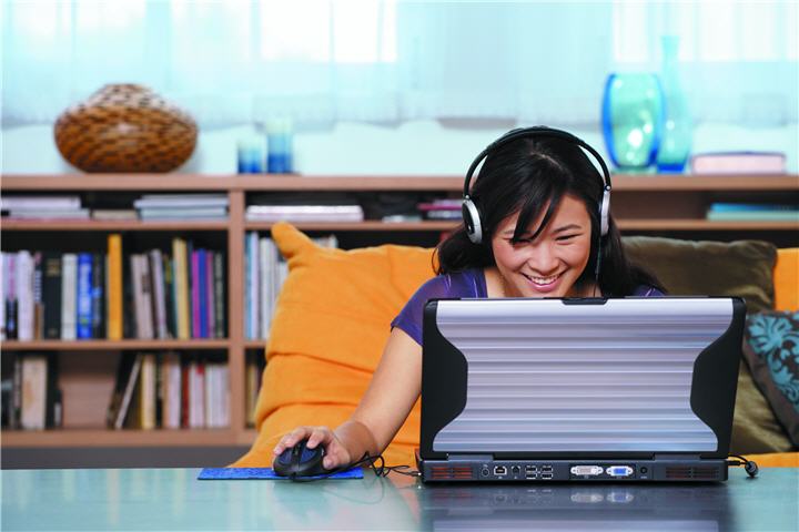 asian woman sitting at a table wearing headphones playing a game on a laptop บทความเรื่อง : สิ่งควรรู้ในการเลือกซื้อคอมพิวเตอร์ (เลือกคอมพิวเตอร์อย่างไรให้ตรงกับการใช้งานมากที่สุด)